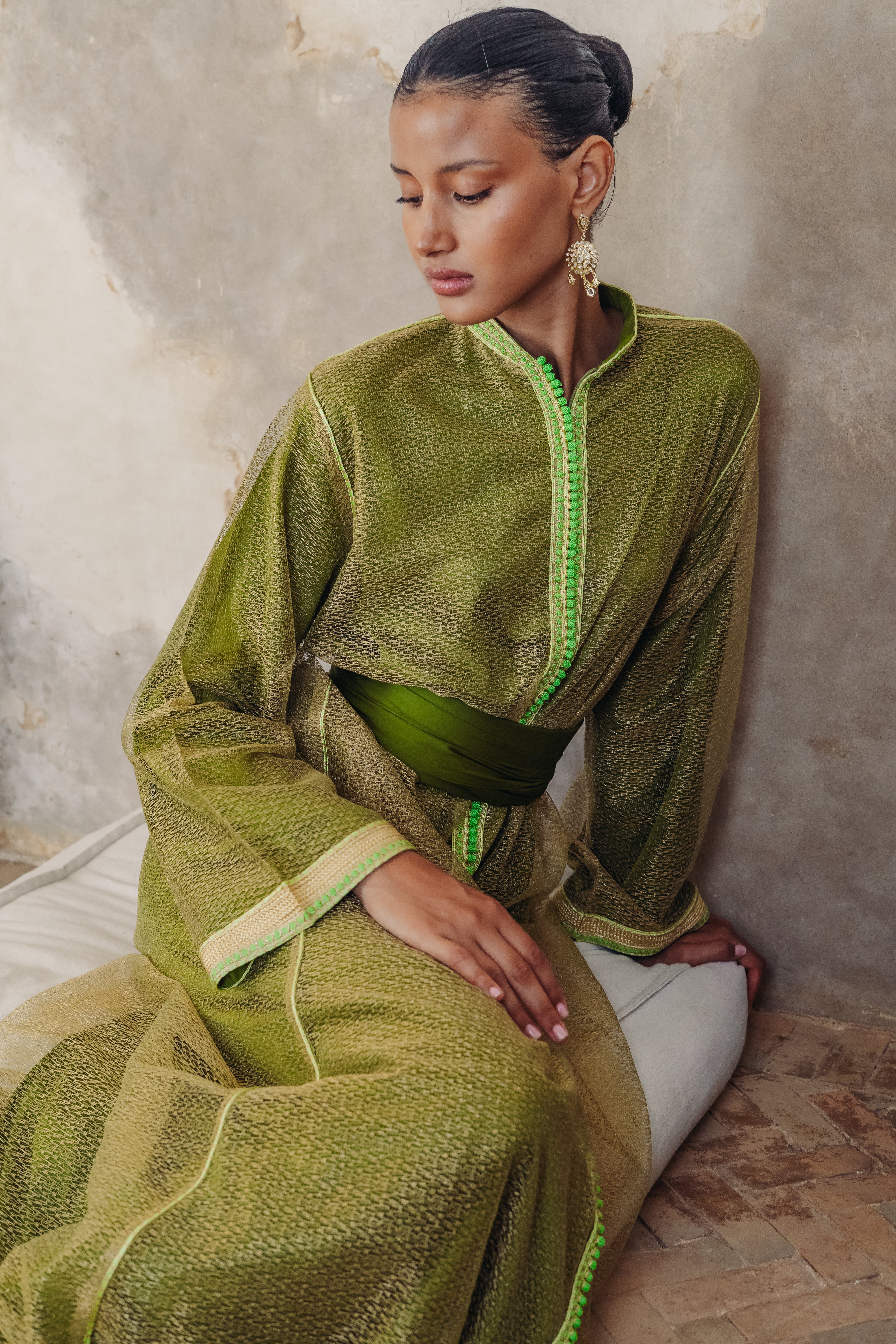 Une femme est assise au sol portant un caftan vert moderne