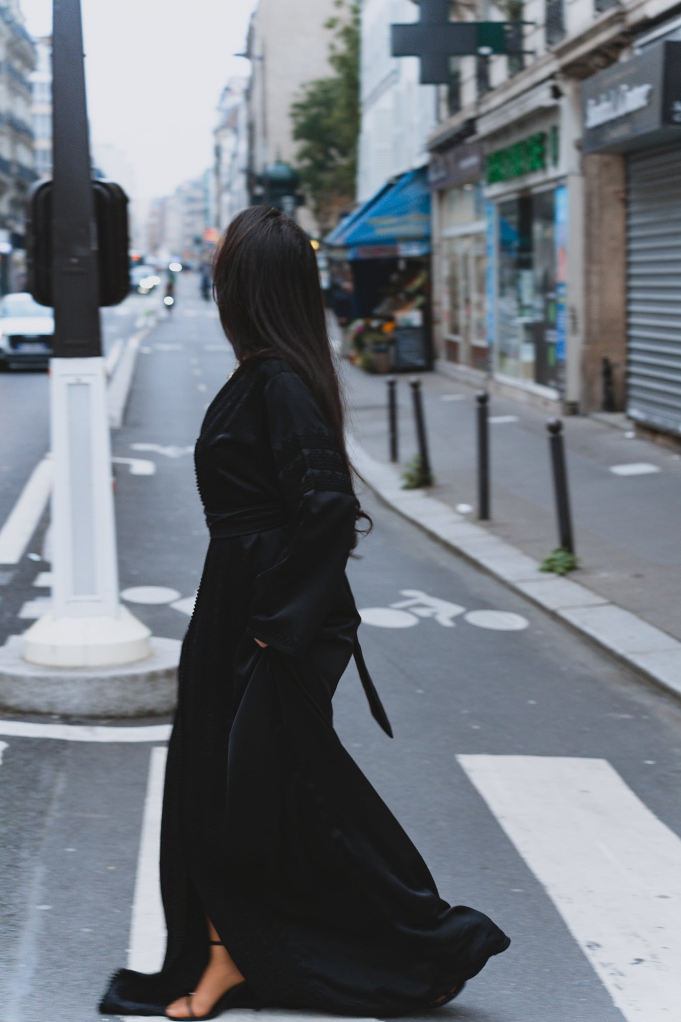 Une femme traverse un passage piéton, elle porte un caftan noir moderne