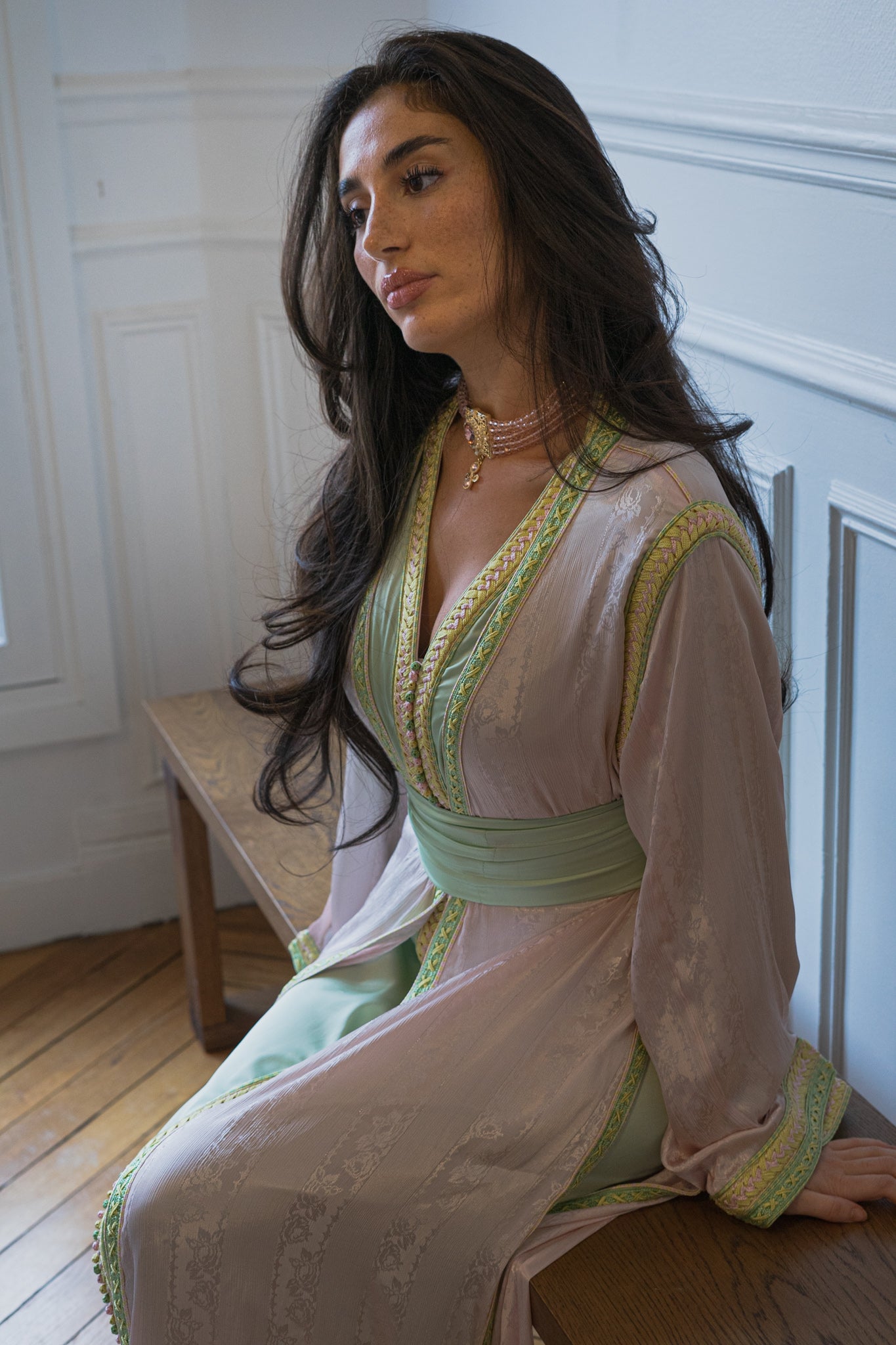 modèle photo qui pose sur un banc et portant une takchita moderne marocaine rose et verte