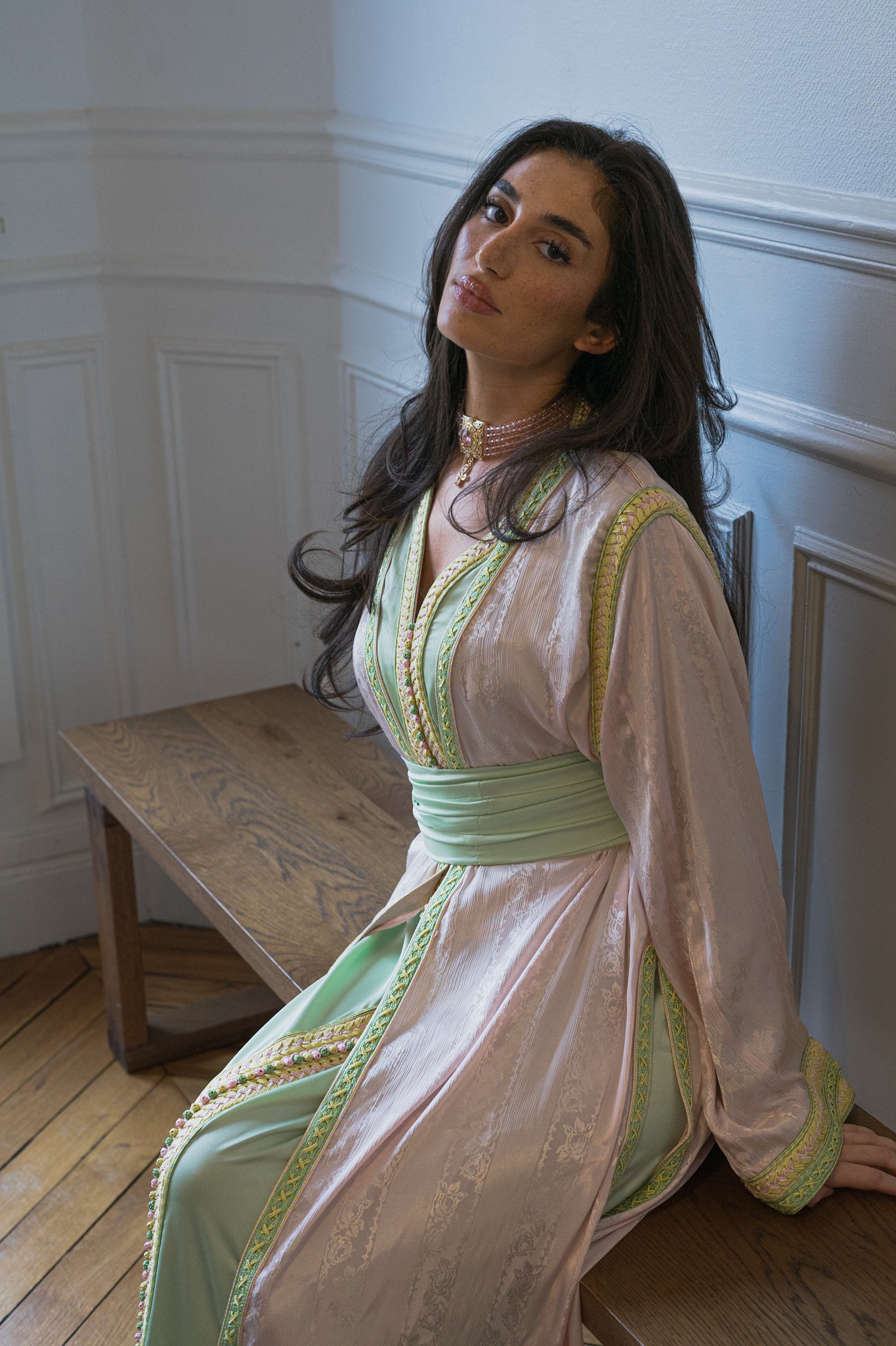 Modèle posé sur un banc et portant une takchita marocaine rose et verte et aux détails jaunes